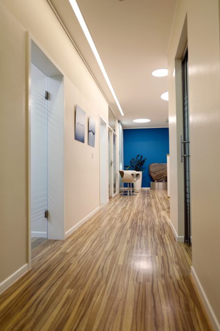 Heller Flur mit Holzfußboden, Bürotüren und einem blauen Akzentwand.