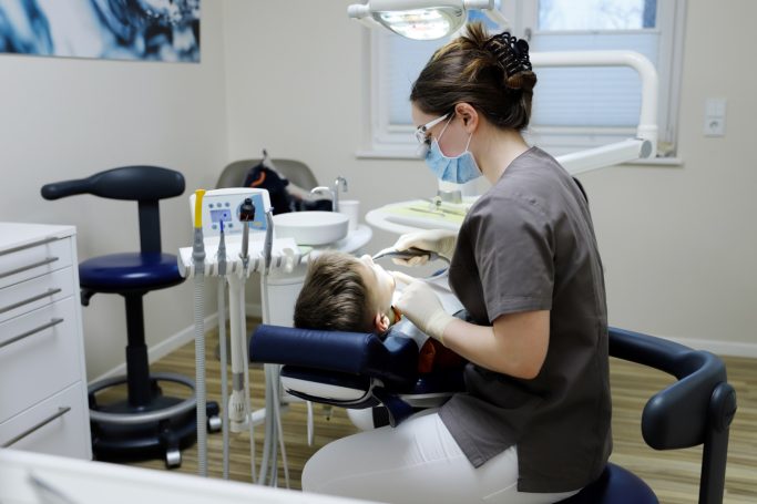 Frau in Zahnarztpraxis behandelt einen Patienten im Behandlungsstuhl.