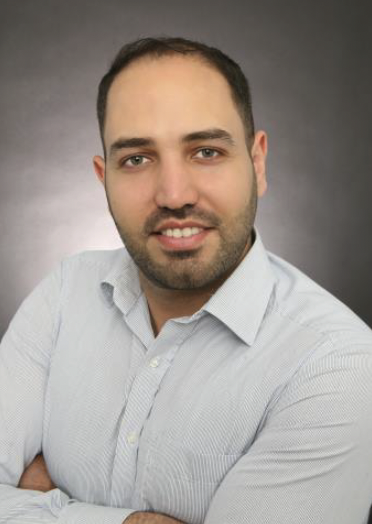 Ein Mann mit kurz geschnittenen Haaren und einem lächelnden Gesicht, gekleidet in ein hellblaues Hemd.