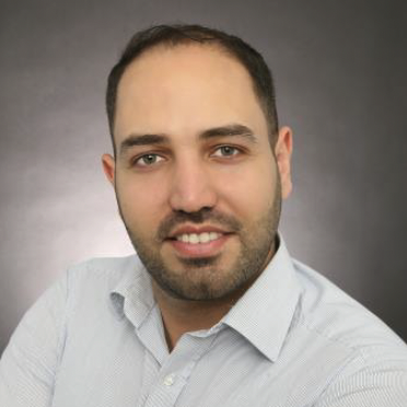 Porträt eines Mannes mit kurzem Bart und lächelndem Gesicht, in einem grauen Hemd.