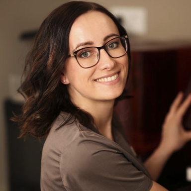 Lächelnde Frau mit Brille, die an einem roten Kühlschrank steht.