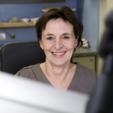 Frau mit kurzen Haaren lächelt freundlich am Schreibtisch.
