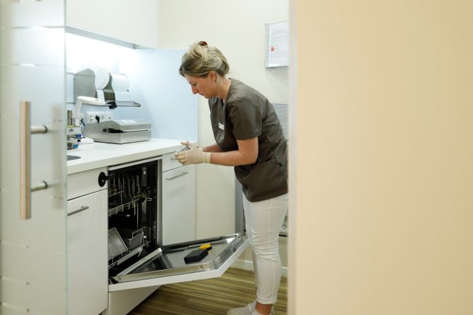 Frau in Küchenuniform reinigt Geschirrspüler in moderner Küche.