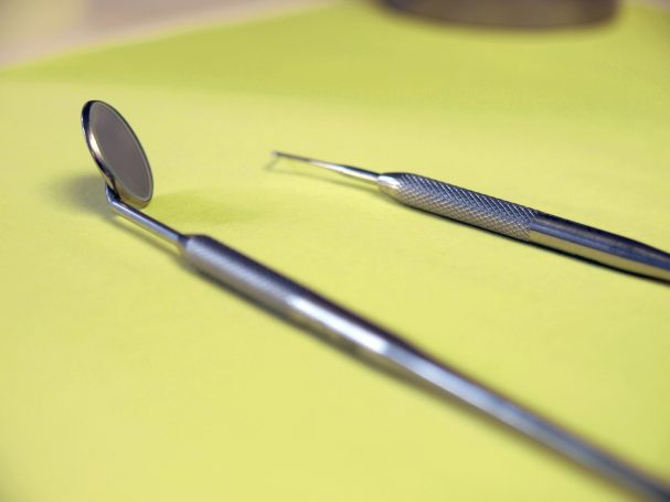 Zahnärztliche Instrumente: Spiegel und Sonde auf gelbem Untergrund.