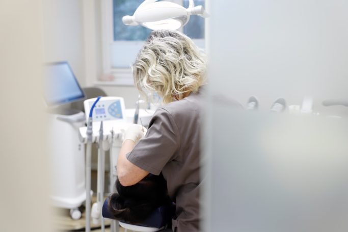 Zahnärztliche Behandlung: Eine Person mit blonder Haar sitzt am Patienten.