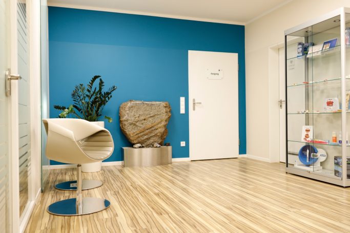 Moderne Empfangshalle mit blauer Wand, Stuhl und Glasvitrine. Pflanzen dekorieren den Raum.