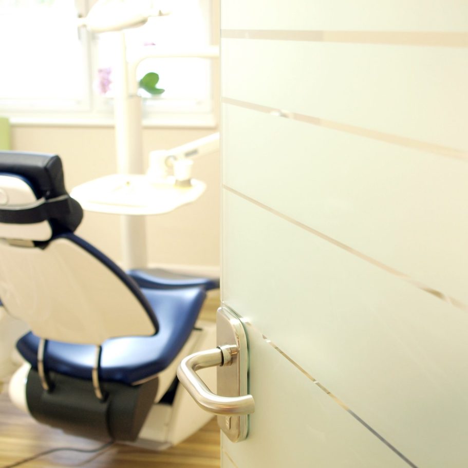 Zahnarztpraxis mit einem blauen Behandlungsstuhl und einer Tür im Vordergrund.
