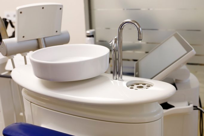 Aufbereitungsbereich mit Spülbecken und modernem Monitor für zahnmedizinische Behandlungen.